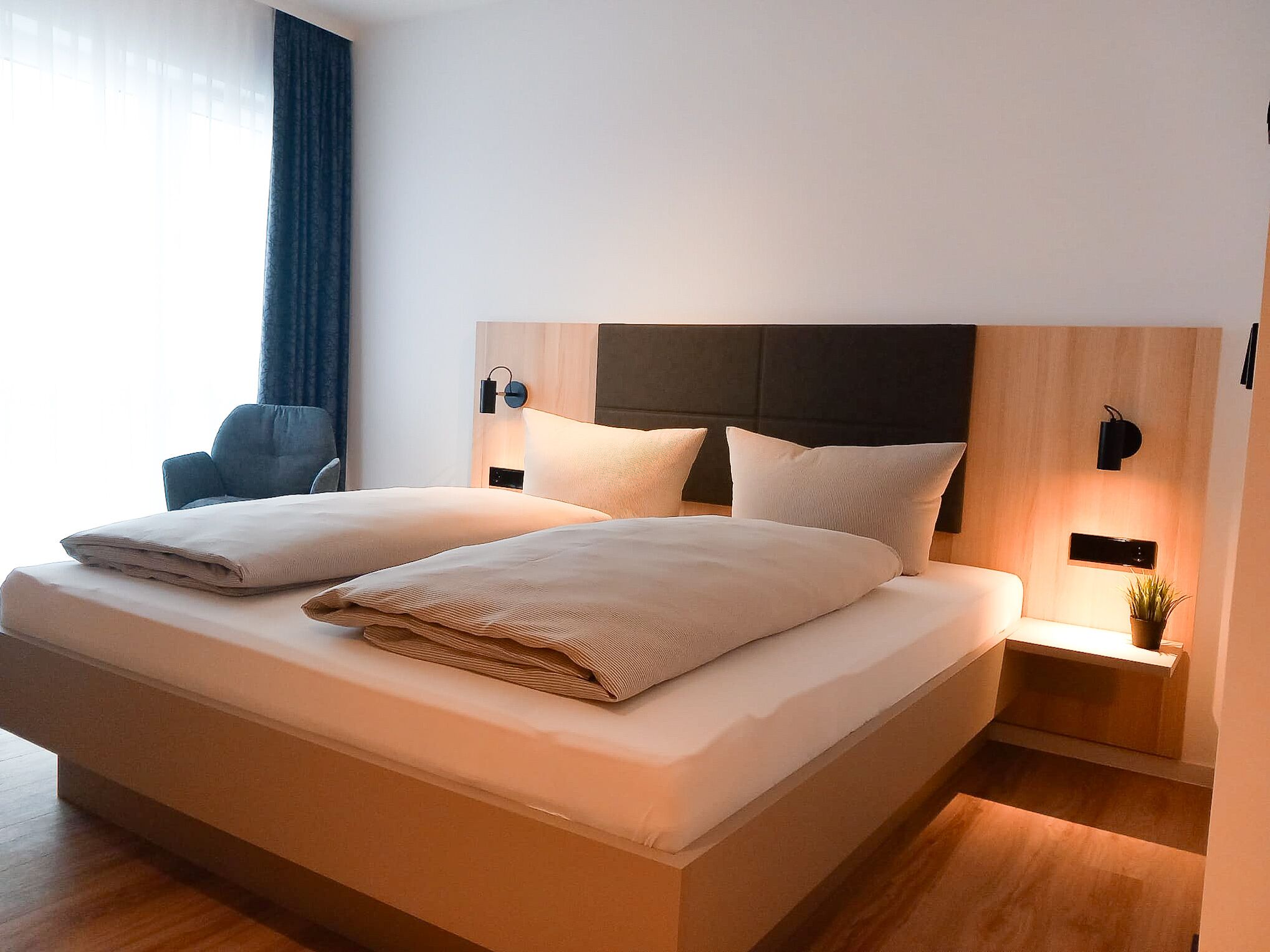 Une chambre d’hôtel moderne avec un grand lit, deux tables de chevet, une chaise et une plante en pot.