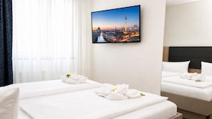 Ein Hotelzimmer mit zwei Betten, weißen Laken und Handtüchern mit Blumen. An der Wand hängt ein Stadtbild.