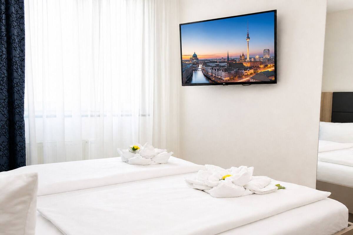 A hotel room with two beds, white linens, and towels with flowers. A cityscape painting is on the wall.