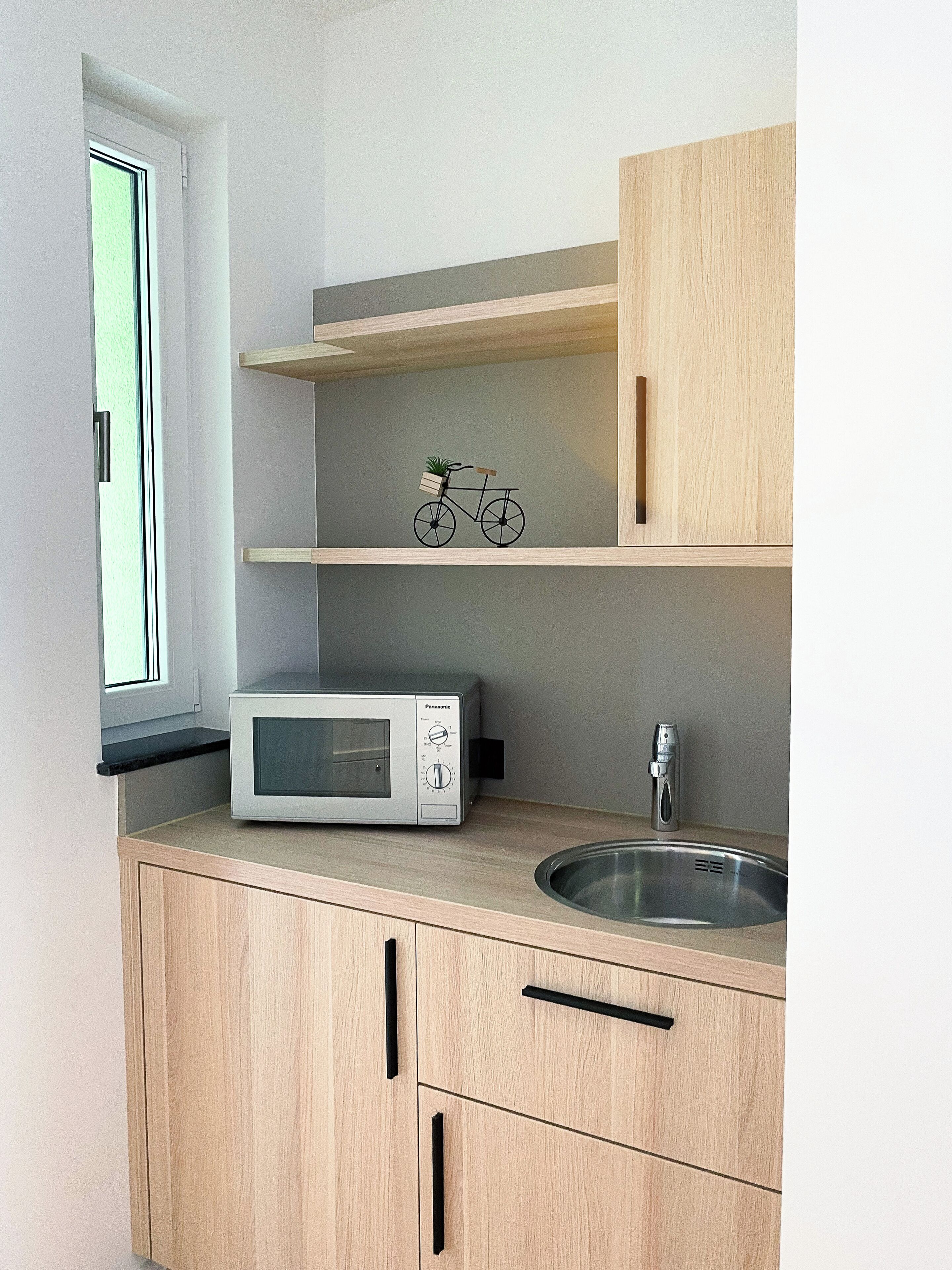 Una cocina compacta con microondas, pileta y muebles de madera.