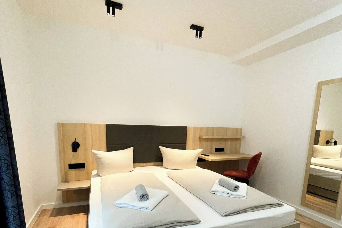 A modern bedroom with a large bed, bedside tables, a mirror, and a red chair.