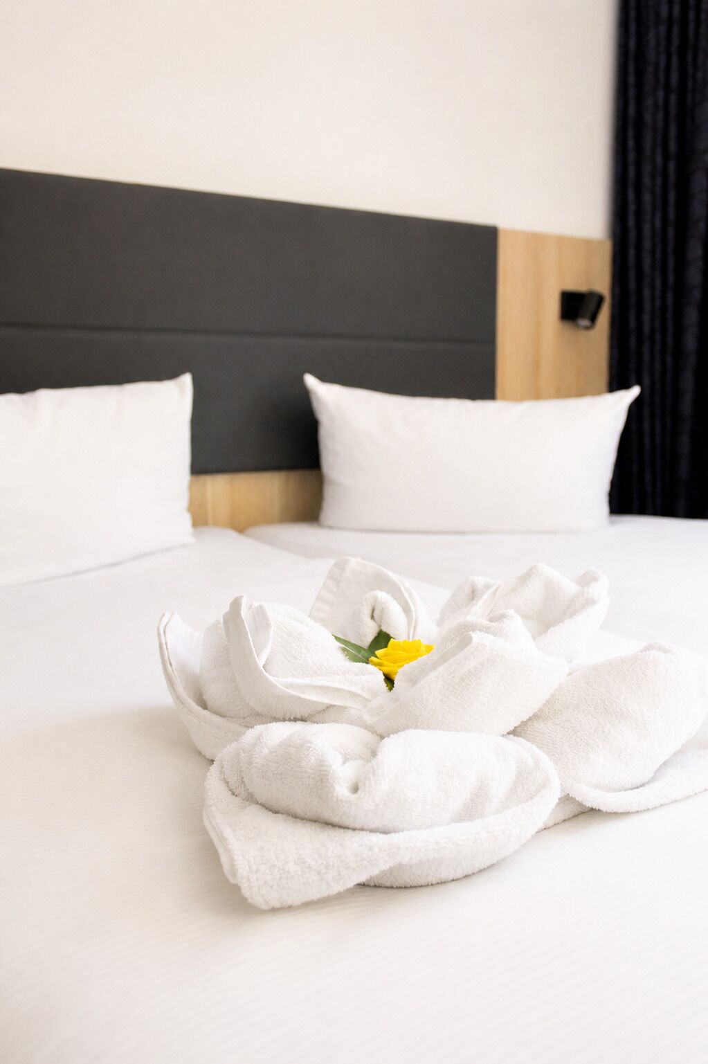 Cama bem arrumada com lençóis brancos e uma única flor amarela.