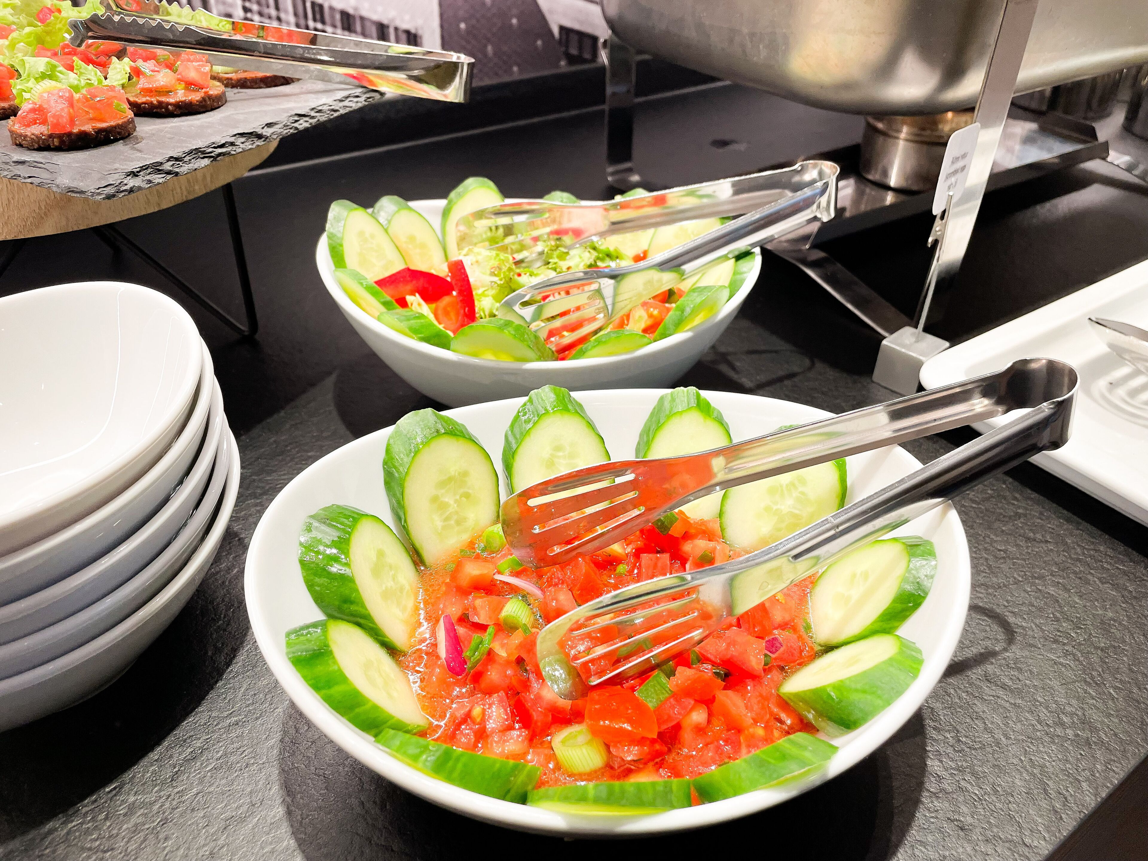 Ein reichhaltiges Buffet mit verschiedenen Speisen, darunter ein Gurkensalat und eine Schale mit roten Tomaten.