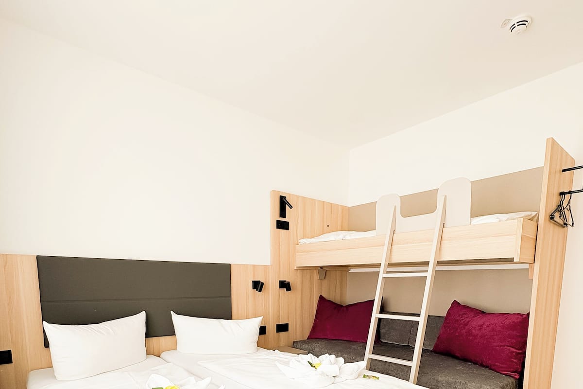A hotel room with a bunk bed, a single bed, a bench, and a small desk.