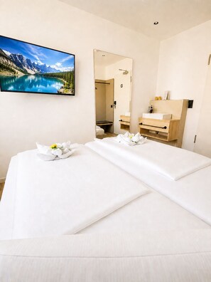 A hotel room with a bed, a bathroom, a large mirror, and a wall-mounted TV displaying a mountain landscape. - HOLI City Apart Hotel Berlin (Berlin)