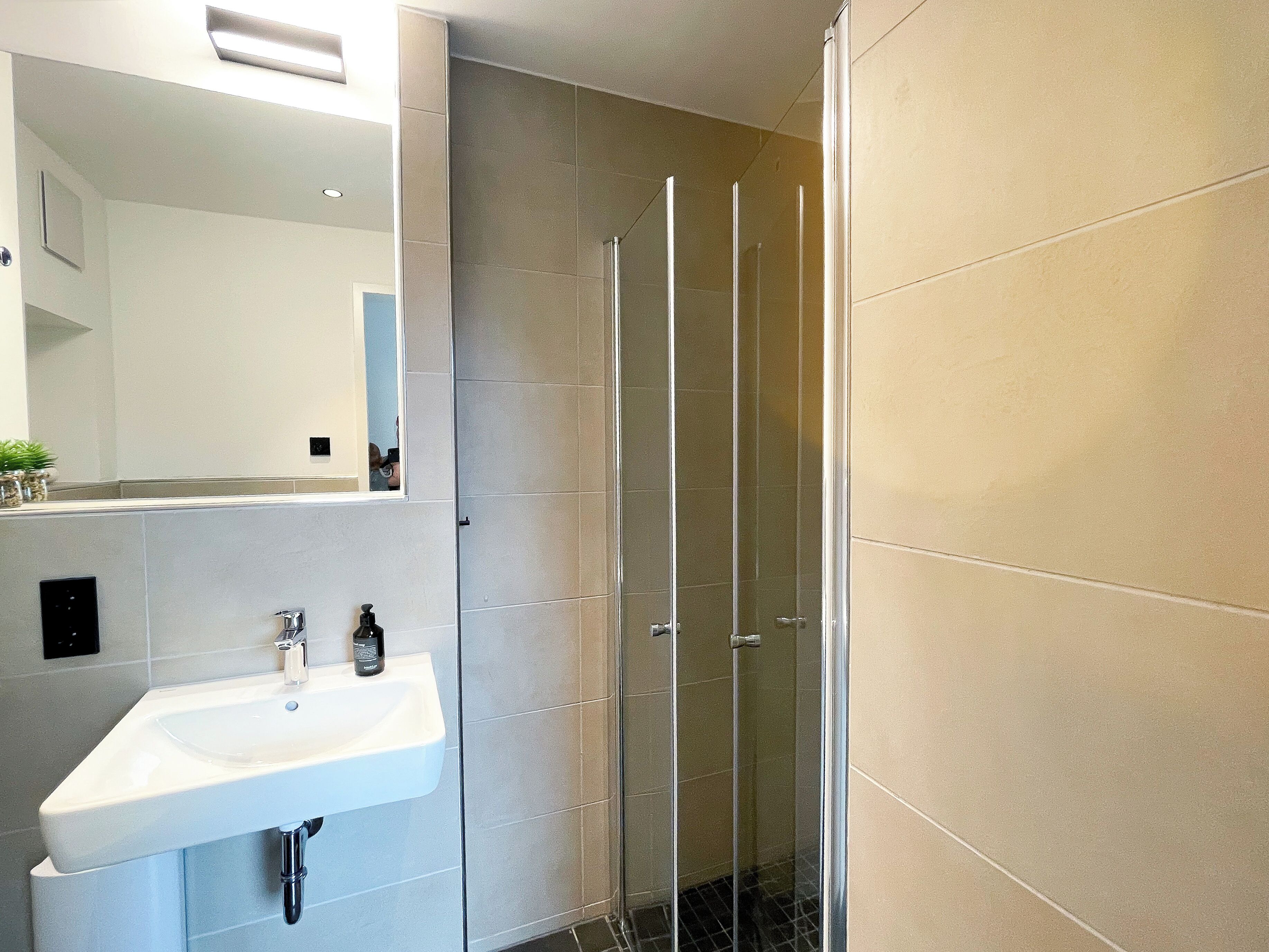 Ein modernes Badezimmer mit einem weißen Waschbecken, einem Spiegel und einer Duschkabine aus Glas.