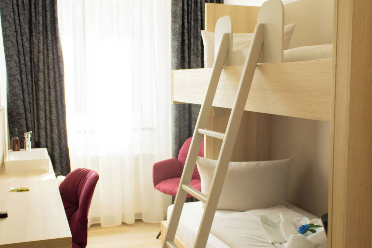 A bunk bed with a ladder, a desk, a chair, and a window with curtains.