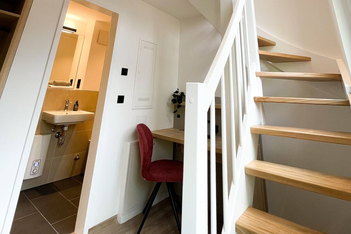 A modern interior with a staircase, a red chair, and a bathroom with a sink and mirror.