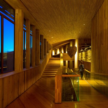 A modern interior with wooden paneling, a glass railing, and a staircase leading to an upper level.