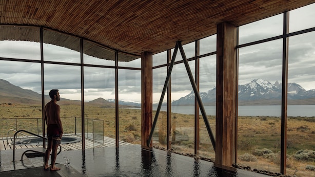 A man standing by a large indoor pool with a view of mountains and a lake.
