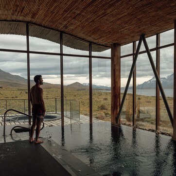 A man standing by a large indoor pool with a view of mountains and a lake.