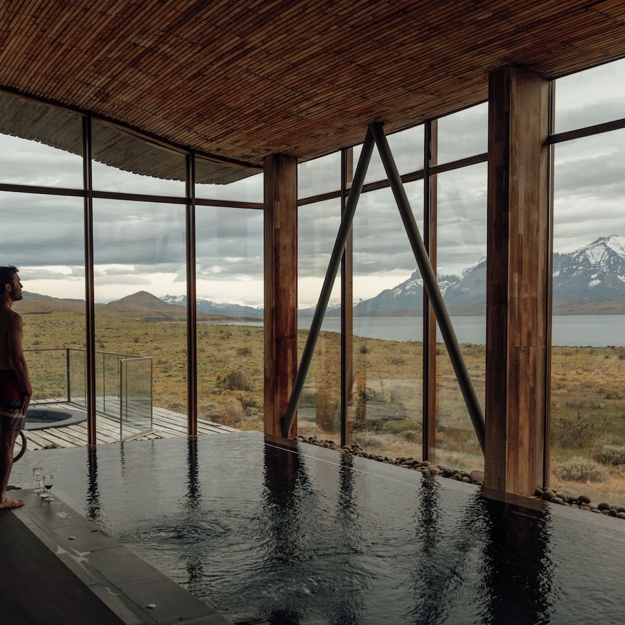 A man standing by a large indoor pool with a view of mountains and a lake.