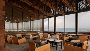 A wooden deck with seating and large windows overlooking a body of water.