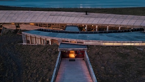 A modern building with a flat roof and a wooden deck leading to a covered entrance.