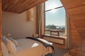A bedroom with a large window, a bed, a bedside table, and a hanging light fixture.