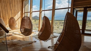 A room with large windows, hanging wicker chairs, and a wooden floor.