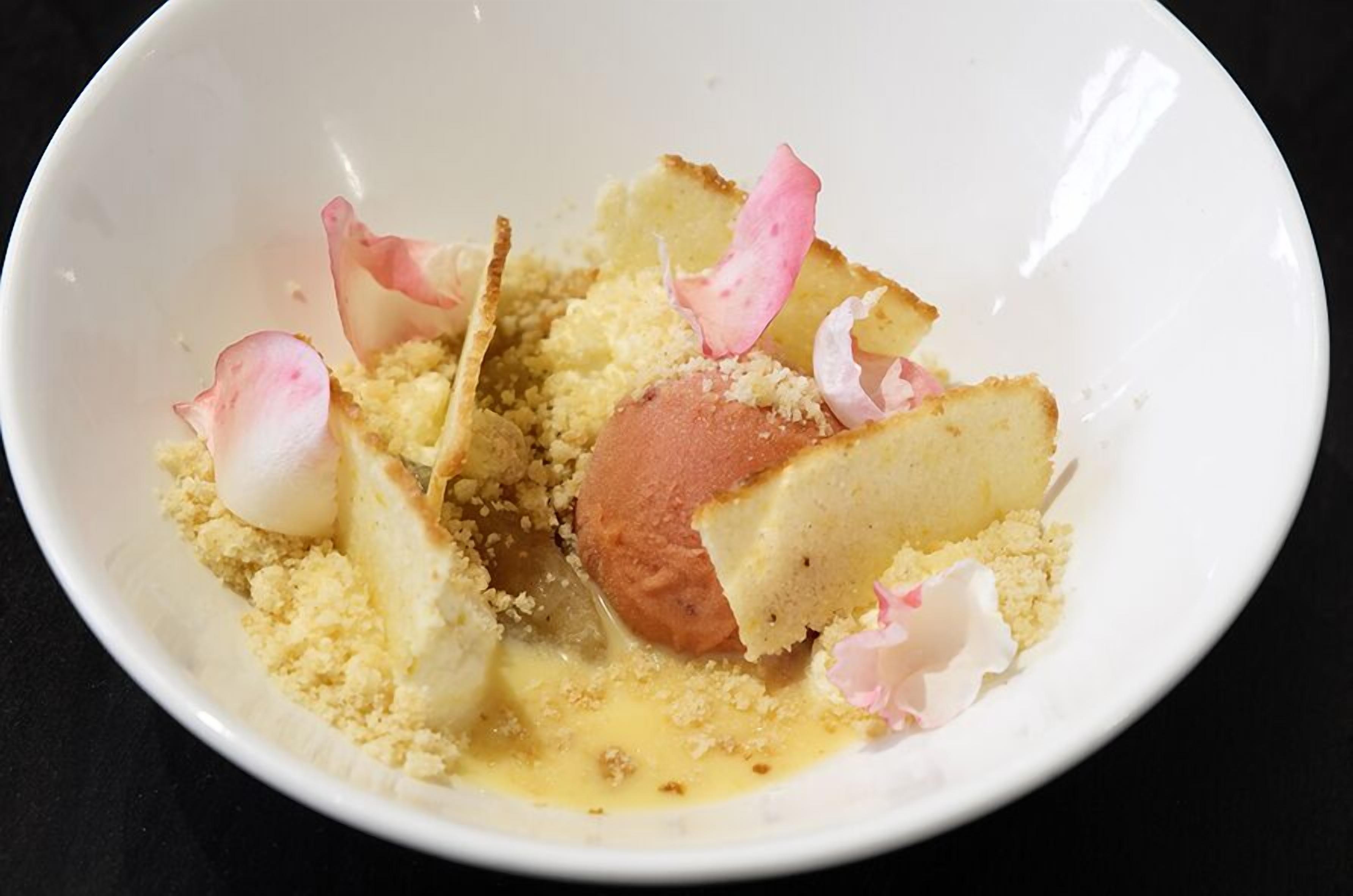 A dessert with crumbled cake and rose petals on a white plate.