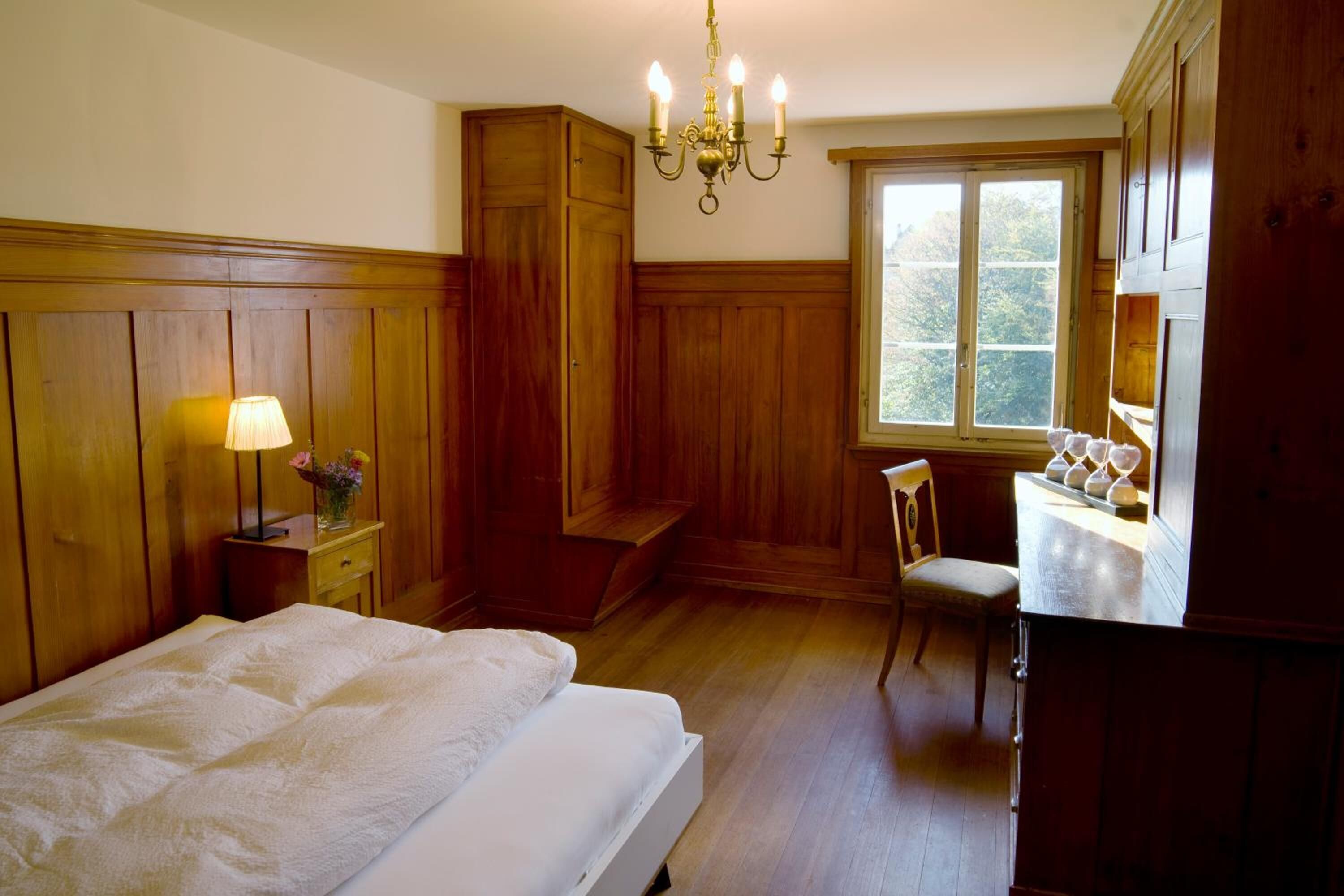 Une chambre à coucher avec un lit, un bureau, une chaise, une lampe et une fenêtre.