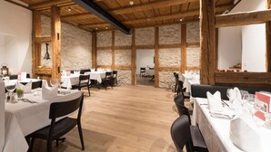 Ein Restaurant mit Holzbalken und Steinwänden, gedeckten Tischen und einer Glocke an der Wand.