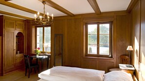 Ein Zimmer mit Holzwänden, einem Bett, einem Schreibtisch und einem Stuhl. Eine Chandelier hängt von der Decke.