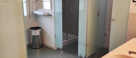 A bathroom with a sink, a mirror, a trash bin, and a shower stall.
