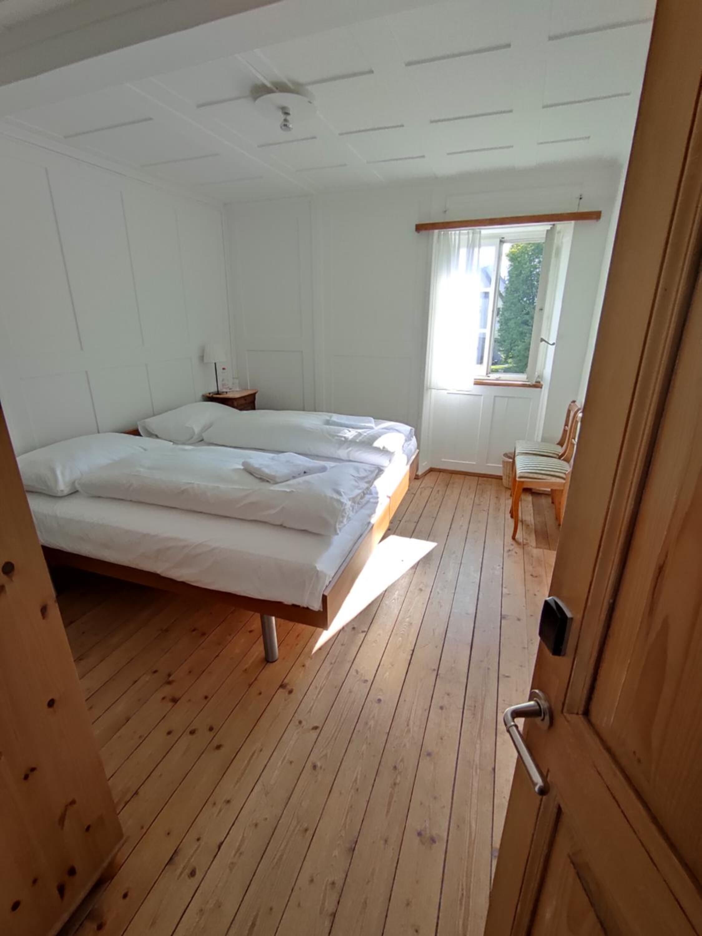 Een kamer met twee bedden, houten vloeren, een raam met gordijnen en een deur.