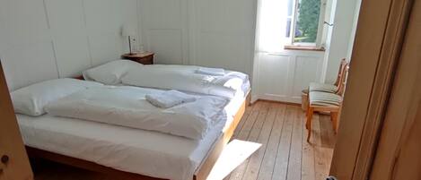 Een kamer met twee bedden, houten vloeren, een raam met gordijnen en een deur.