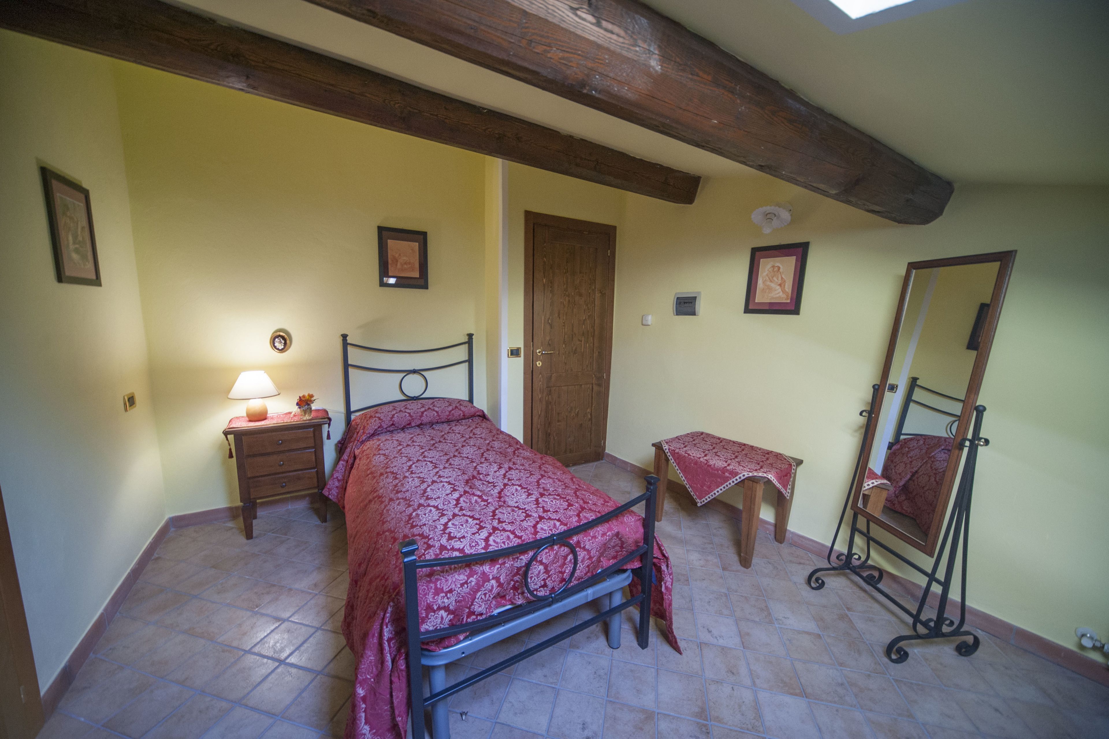 A bedroom with a bed, bedside table, lamp, and a mirror.