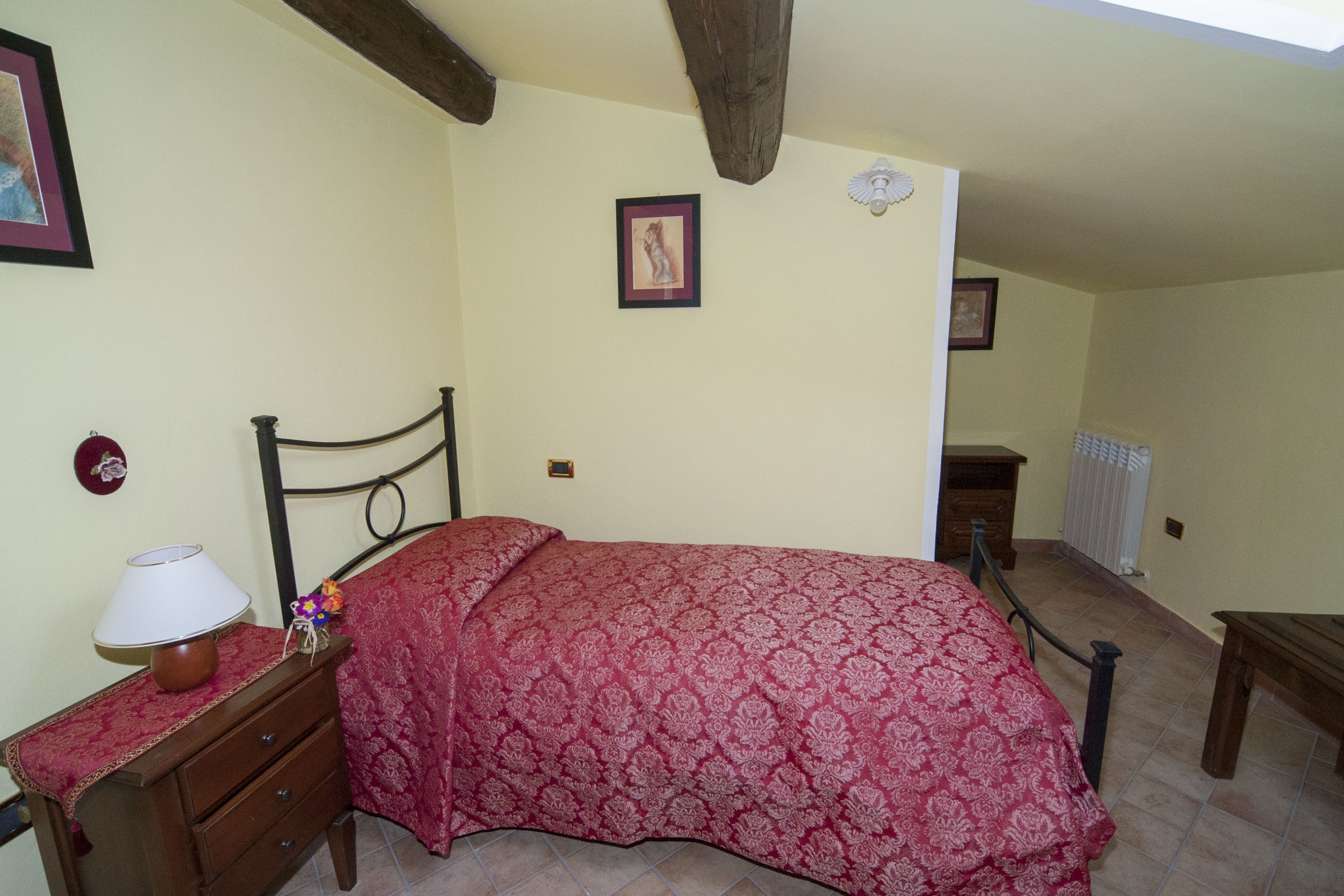 A bedroom with a bed, a nightstand, a lamp, and a picture frame on the wall.
