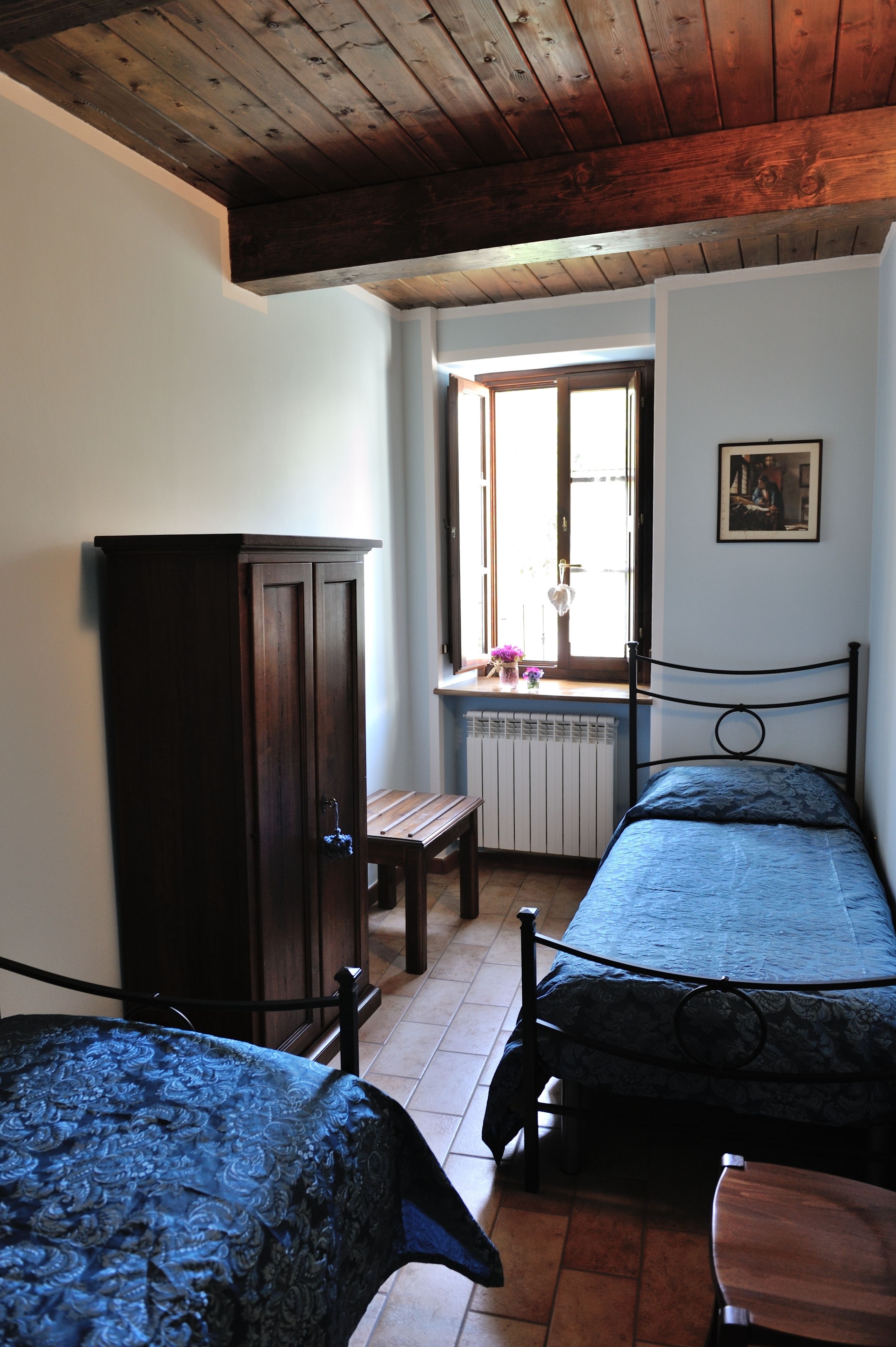 A bedroom with two single beds, a wooden wardrobe, a bench, and a window with a view.