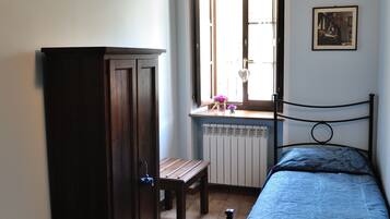 A bedroom with two single beds, a wooden wardrobe, a bench, and a window with a view.