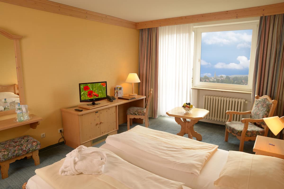 Habitación de hotel con dos camas, un escritorio con computadora, una silla, una mesita y una ventana con vistas.