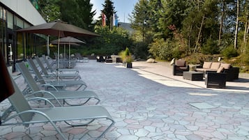 A patio area with lounge chairs and umbrellas, surrounded by trees and a building with large windows.