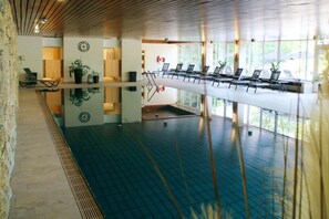 A spacious indoor swimming pool with lounge chairs and potted plants. - Hotel Kaiseralm (Bischofsgruen)
