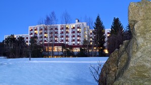 A multi-story hotel with a red and white facade, surrounded by snow and trees. - Hotel Kaiseralm (Bischofsgruen)