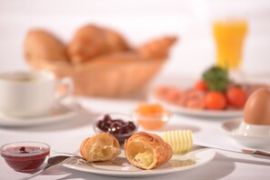 A breakfast setting with croissants, jam, butter, and a glass of orange juice. - Hotel Kaiseralm (Bischofsgruen)