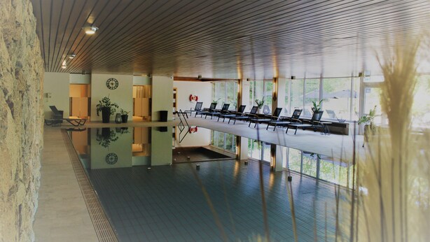 A modern indoor space with a long bench, chairs, and a glass wall. - Hotel Kaiseralm (Bischofsgruen)
