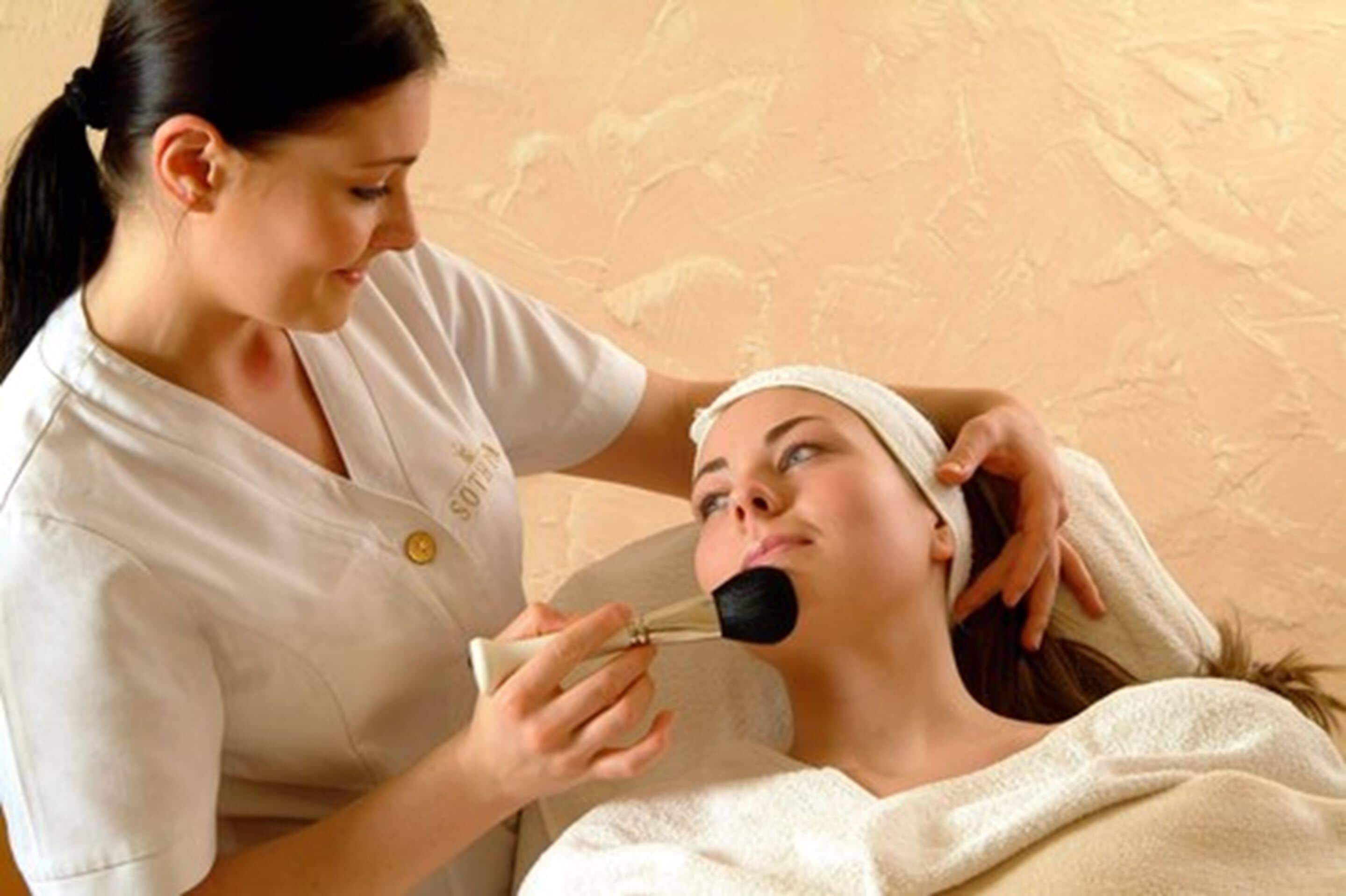 A person receiving a facial treatment in a room with a textured wall.