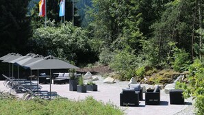 An outdoor seating area with umbrellas, lounge chairs, and planters. - Hotel Kaiseralm (Bischofsgruen)