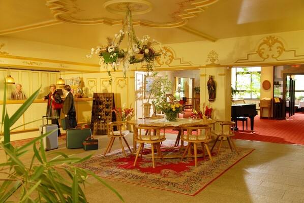 A hotel lobby with a round wooden table, chairs, a chandelier, and a red carpet. - Hotel Kaiseralm (Bischofsgruen)