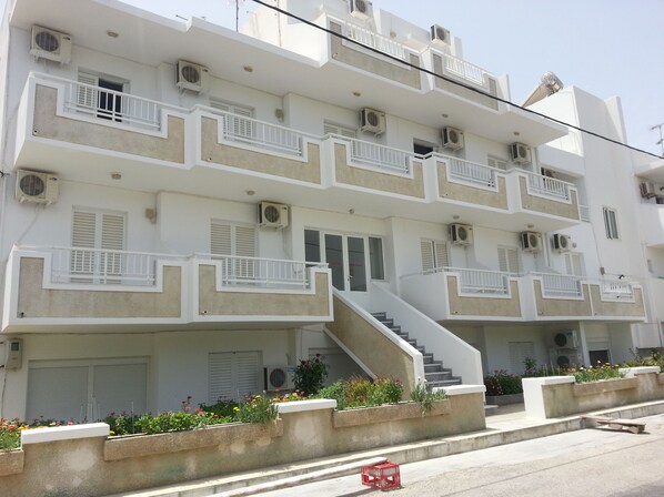 Un edificio de varios pisos con balcones, unidades de aire acondicionado y una escalera que lleva a la entrada.
