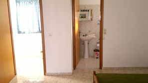 Habitación con baño que incluye lavamanos e inodoro. Hay una puerta que da a otra habitación.