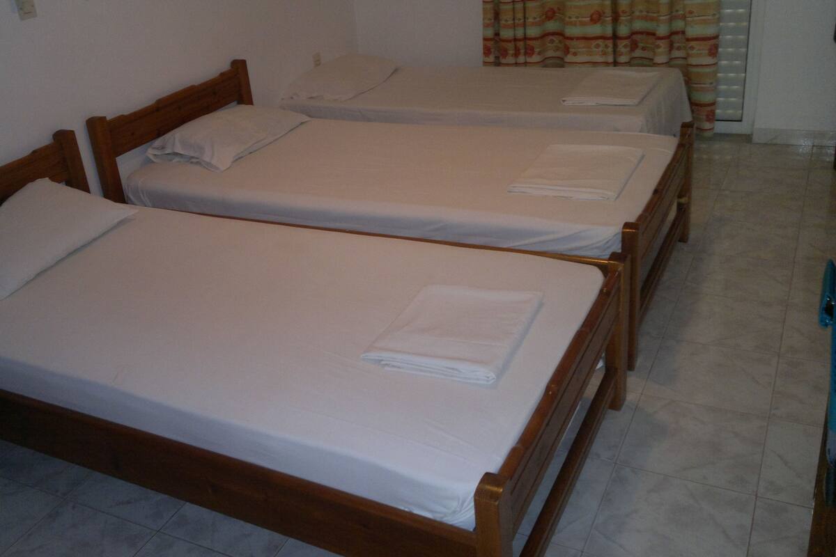 A room with three wooden beds, each with white linens and pillows.