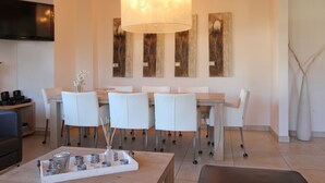 A modern dining area with a large table, white chairs, and a ceiling light fixture. - AvenidA Residenz Burg by Alpin Rentals (Kaprun)