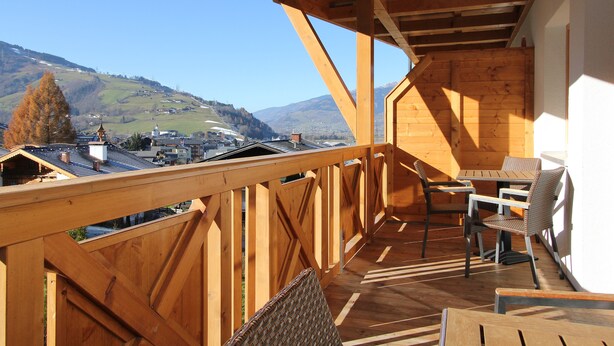 A wooden deck with a table and chairs, overlooking a mountainous landscape. - AvenidA Residenz Burg by Alpin Rentals (Kaprun)