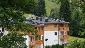 A multi-story building with balconies, satellite dishes, and a view of a green hillside. - AvenidA Residenz Burg by Alpin Rentals (Kaprun)