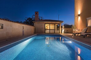 A swimming pool with a tiled deck and a covered area with chairs and a table. - Villa Mihaela (Fazana)