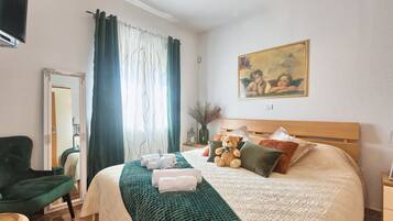 Une chambre à coucher bien rangée, avec un lit, un fauteuil vert, une table de chevet avec une lampe et un tableau accroché au mur.