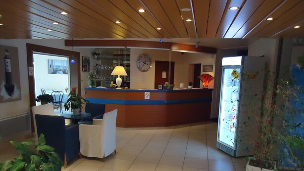 A reception area with a counter, chairs, a clock, and potted plants. - L'Estuaire (Saint-Brevin-les-Pins)