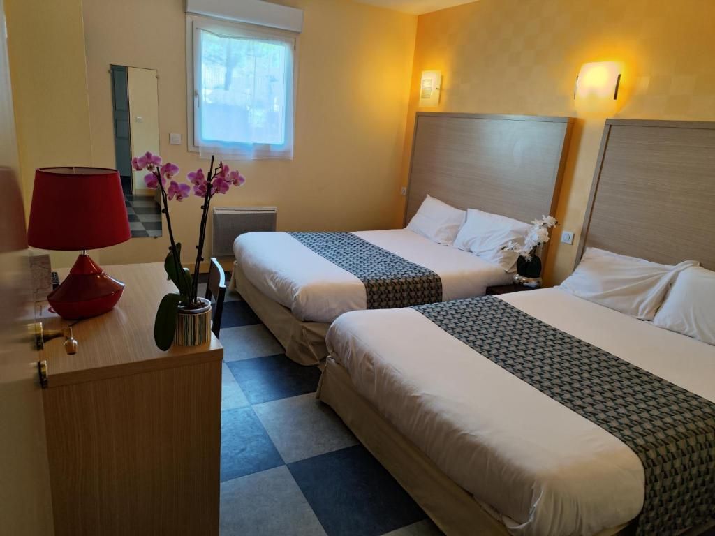 Hotellihuone, jossa on kaksi sänkyä, punainen lamppu, maljakko kukkineen ja ruutukuviollinen lattia.